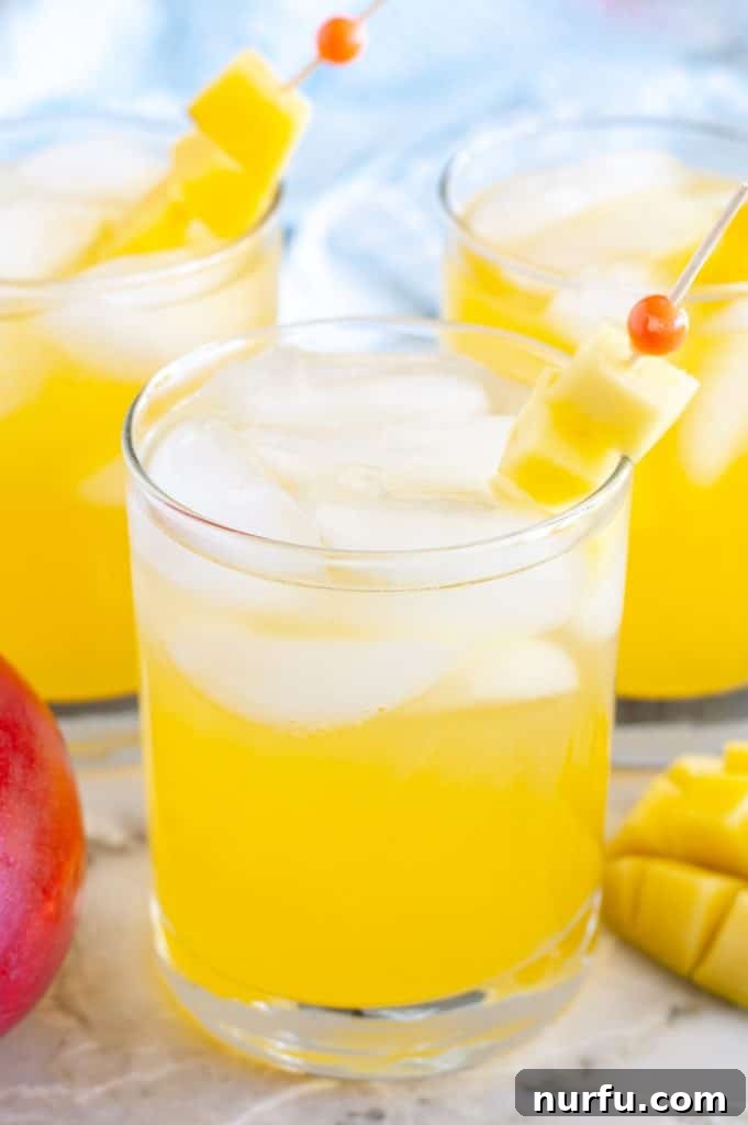 A vibrant glass of mango vodka cocktail, garnished with fresh mango slices, reflecting light on a warm day. The background hints at a tropical setting, inviting a refreshing experience.