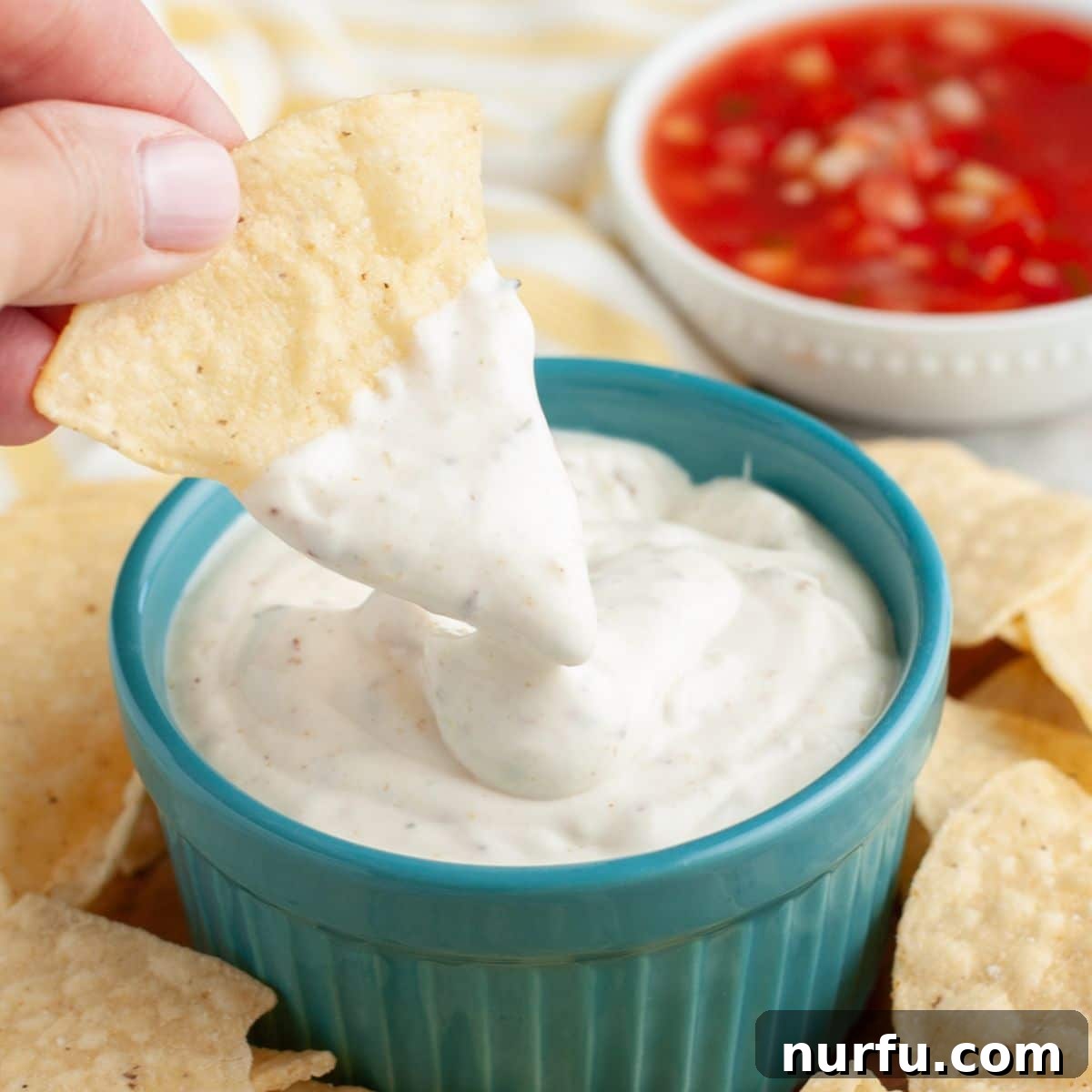 Creamy Mexican Restaurant White Sauce 2 A bowl of creamy Mexican white sauce, a bowl of red salsa, and a pile of crispy tortilla chips on a rustic wooden table.