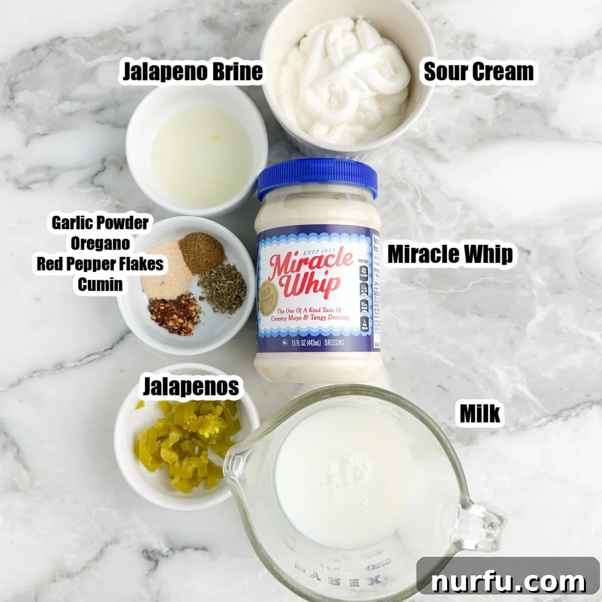 Creamy Mexican Restaurant White Sauce 3 Arrangement of ingredients for Mexican white sauce: a bowl of sour cream, a jar of Miracle Whip, a glass of milk, various spices including garlic powder, cumin, oregano, crushed red pepper, and a bowl of sliced pickled jalapeños.