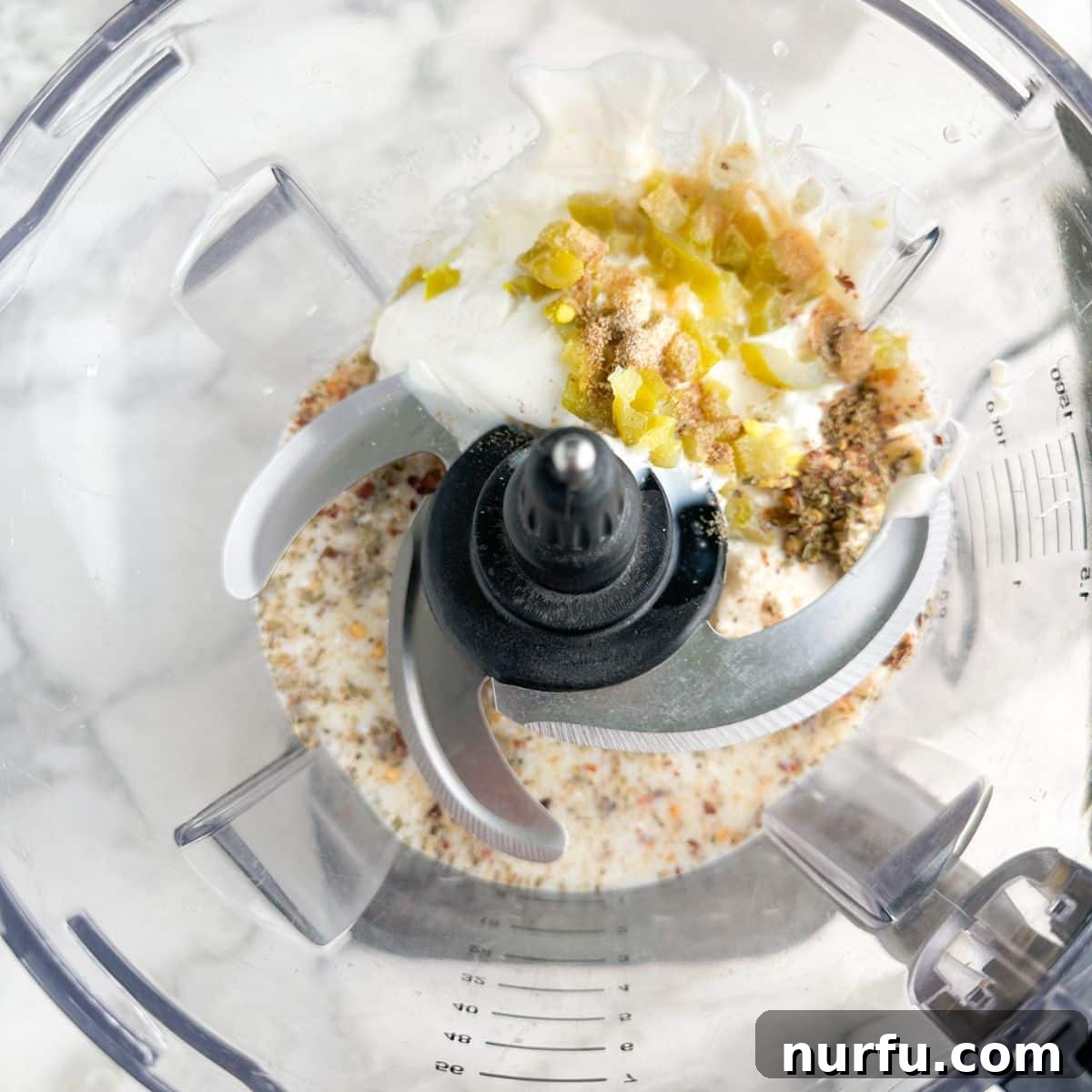 Creamy Mexican Restaurant White Sauce 4 Ingredients for Mexican white sauce, including mayonnaise, spices, milk, and jalapenos, being added to a food processor.