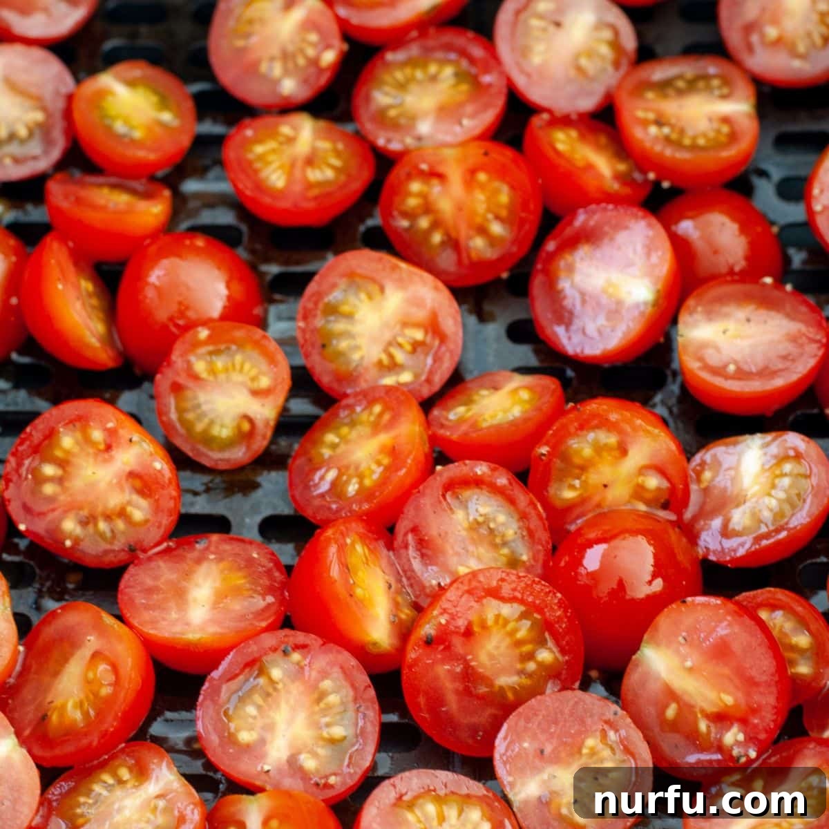 Air Fried Tomato Bites 5 Halved cherry tomatoes arranged in a single layer within an air fryer basket, showing a beautiful contrast against the dark metal.