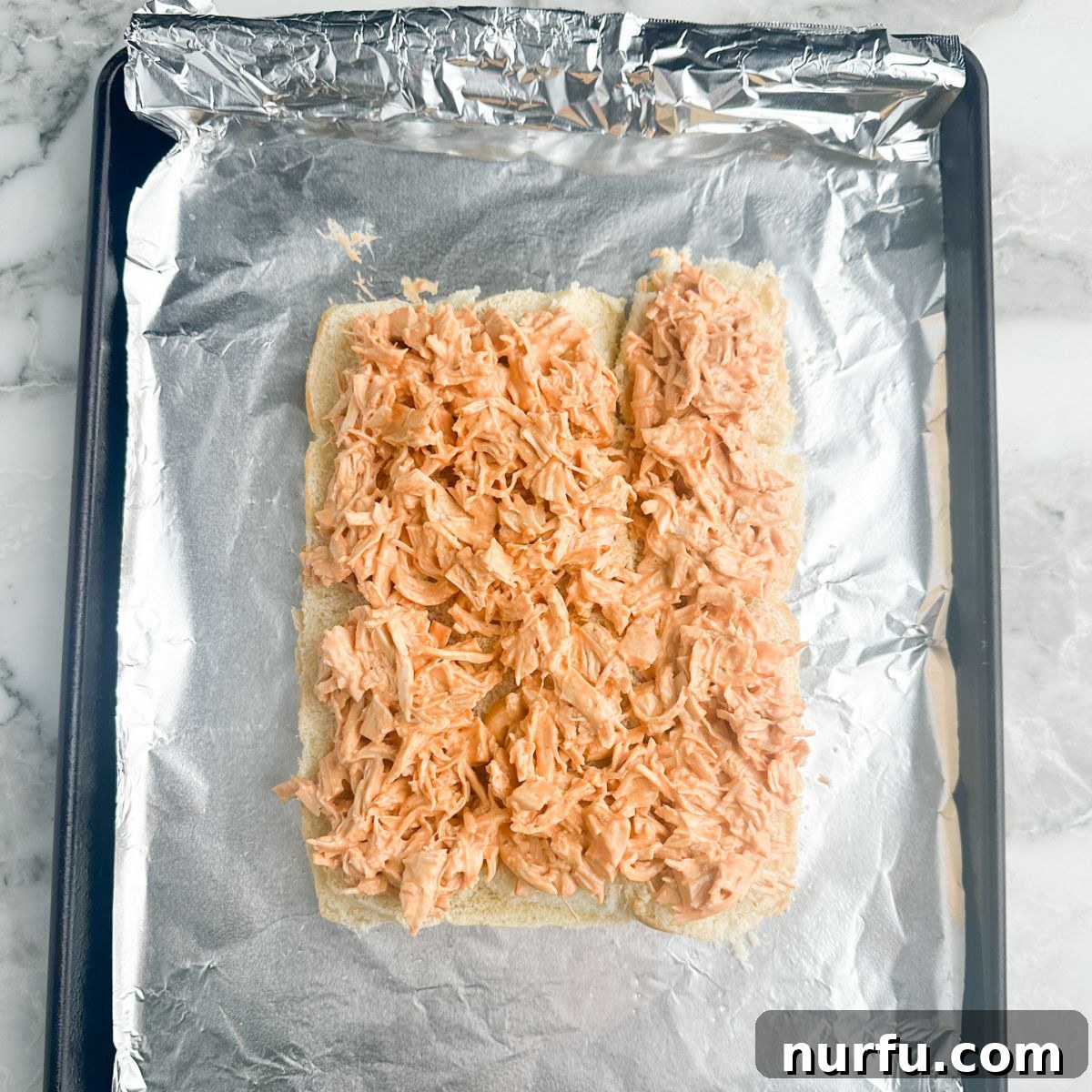 Shredded buffalo ranch chicken mixture spread evenly over the bottom halves of Hawaiian rolls.