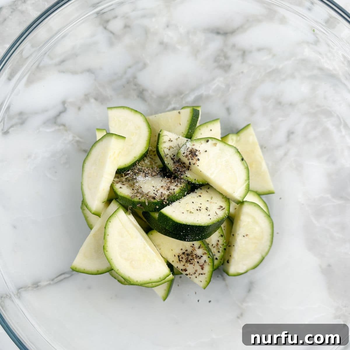 A mixing bowl filled with perfectly sliced zucchini, seasoned with salt and pepper, ready for the air fryer.