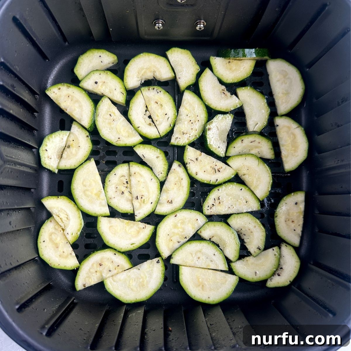 Uniformly sliced and seasoned zucchini arranged in a single layer inside an air fryer basket, ready for cooking.