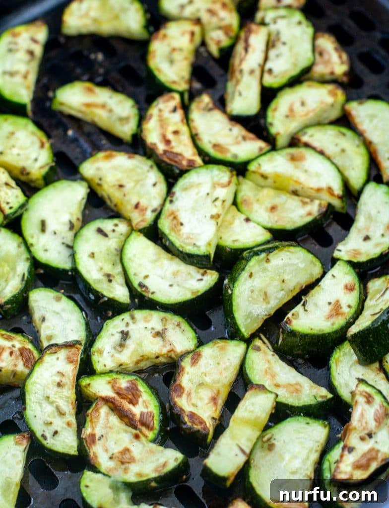 Perfectly roasted, golden-brown zucchini pieces cooling slightly in the air fryer basket after cooking.