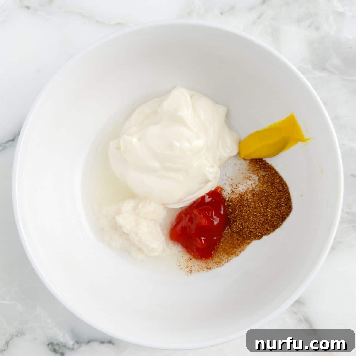 Burger King Signature Zesty Dip 4 A mixing bowl containing mayonnaise, ketchup, mustard, and various seasonings, just beginning to be stirred.