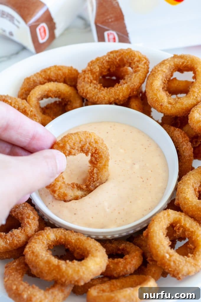 Burger King Signature Zesty Dip 6 A hand dipping a perfectly golden onion ring into a bowl of creamy Burger King Zesty Sauce.