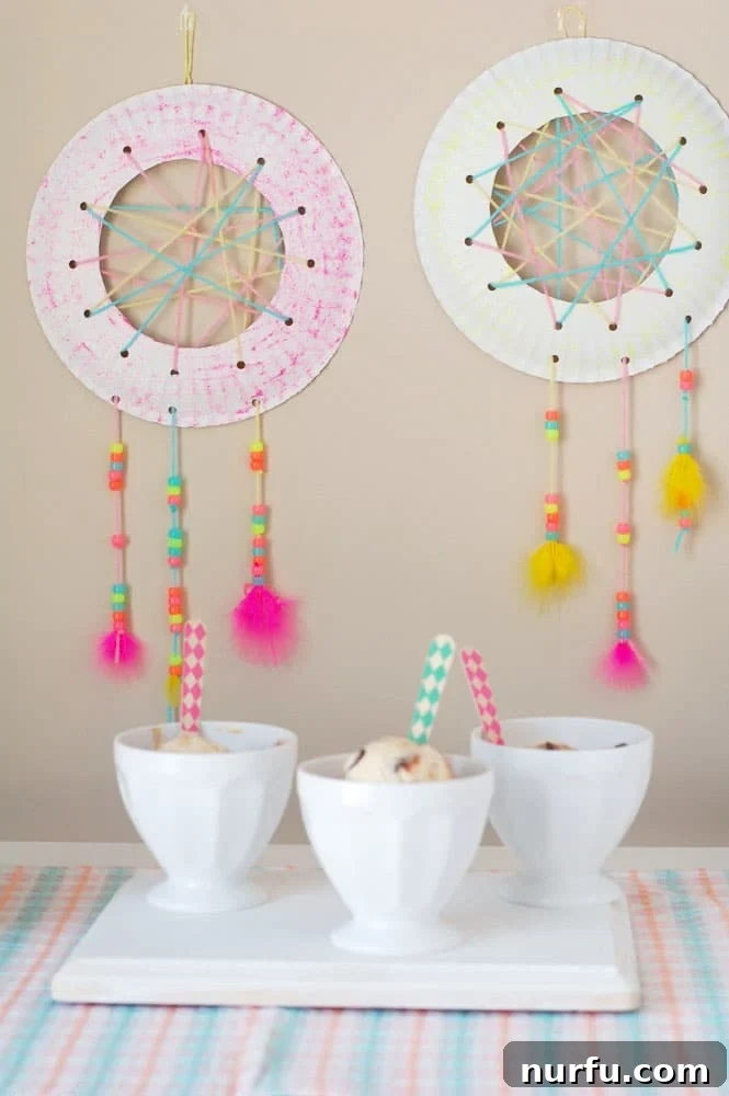 A beautifully handmade DIY dream catcher, crafted from a paper plate and adorned with colorful yarn, beads, and feathers, ready to be hung in a child's bedroom to inspire sweet dreams and imaginative play. The perfect kids craft for a creative summer day.