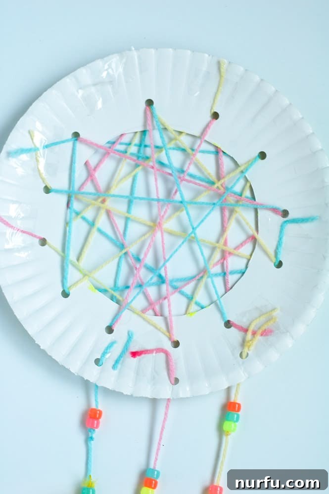 A completed DIY dream catcher, adorned with colorful yarn, beads, and feathers, rests on a wooden table, showcasing its intricate web and decorative hanging elements. This charming craft is ready to inspire sweet dreams.