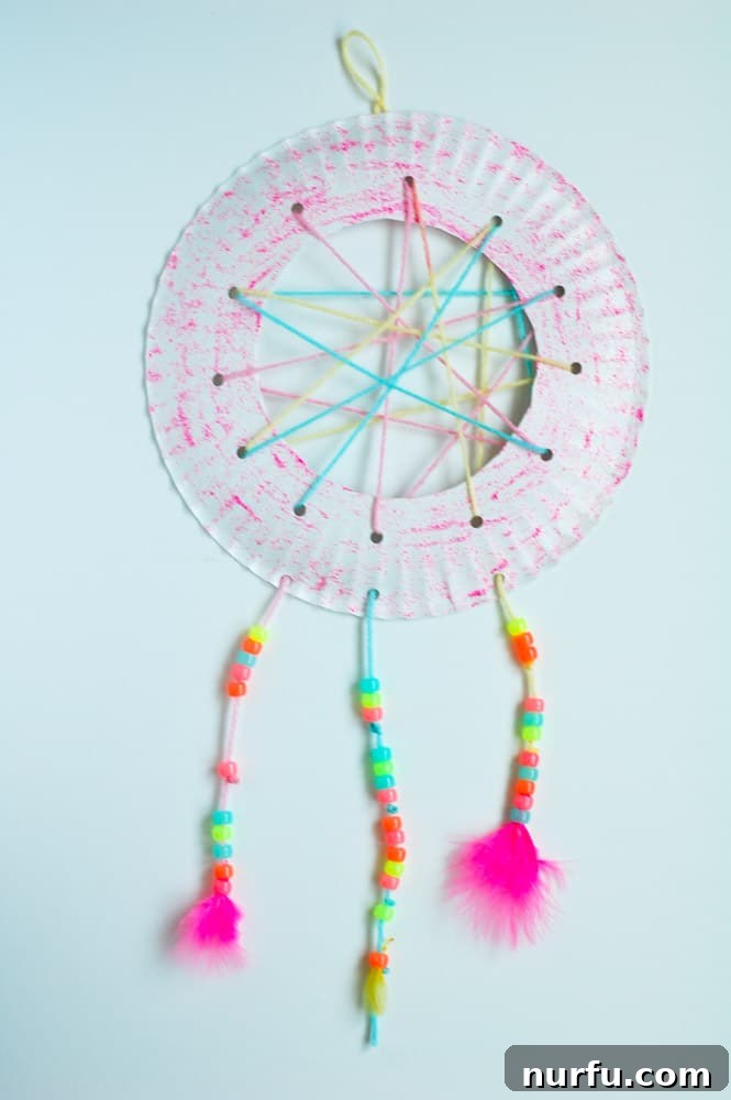 A close-up of a beautifully handcrafted DIY dream catcher, featuring a vibrant paper plate frame, a colorful yarn web, and intricate hanging strands with beads and feathers, ready to bring sweet dreams to a child's room.