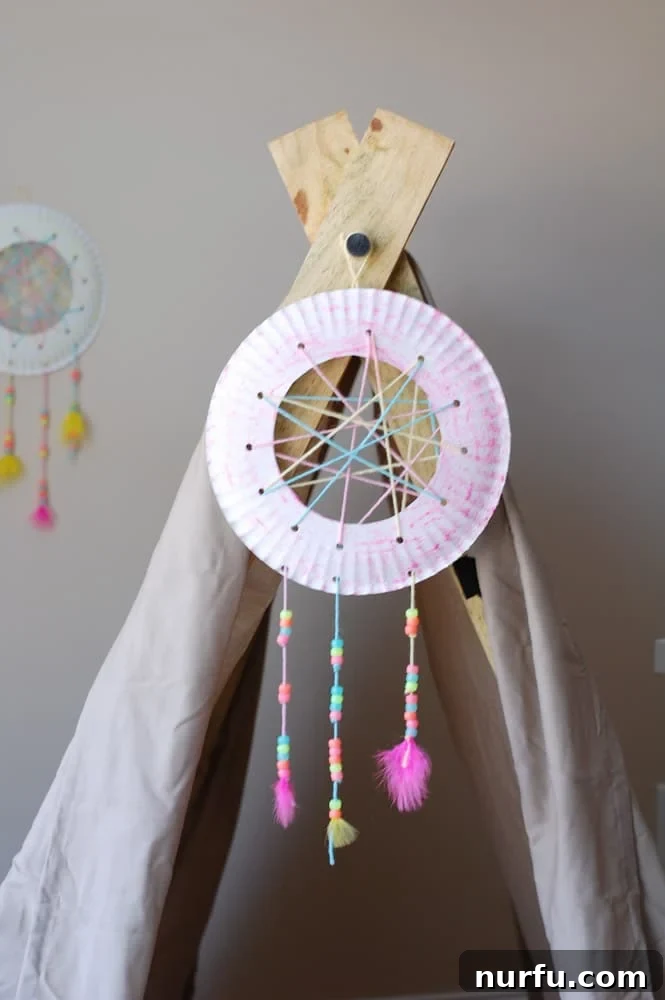 A colorful DIY dream catcher, made by children, gracefully hangs inside a decorative teepee, creating a cozy and magical atmosphere for a glamping themed party. It embodies the joy of a handmade kids' craft.