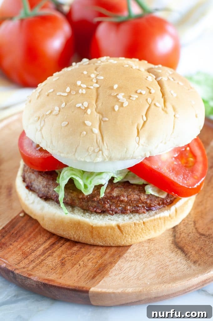 Perfect Air Fryer Frozen Turkey Burgers 2 A perfectly cooked turkey burger on a bun, garnished with fresh tomatoes and lettuce, with additional tomatoes in the background.