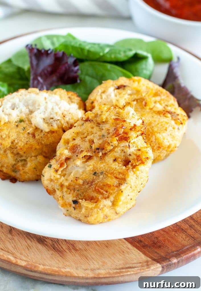 Crispy Air Fryer Frozen Crab Cakes 2 A plate featuring three golden-brown, perfectly cooked crab cakes, garnished with fresh herbs and a lemon wedge, ready to be served.
