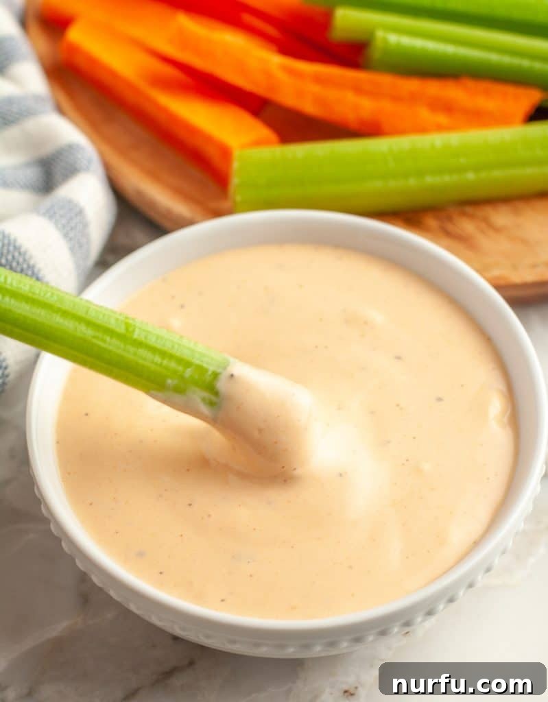 Crisp celery stick being dipped into a bowl of creamy, orange-hued Buffalo Ranch dip.