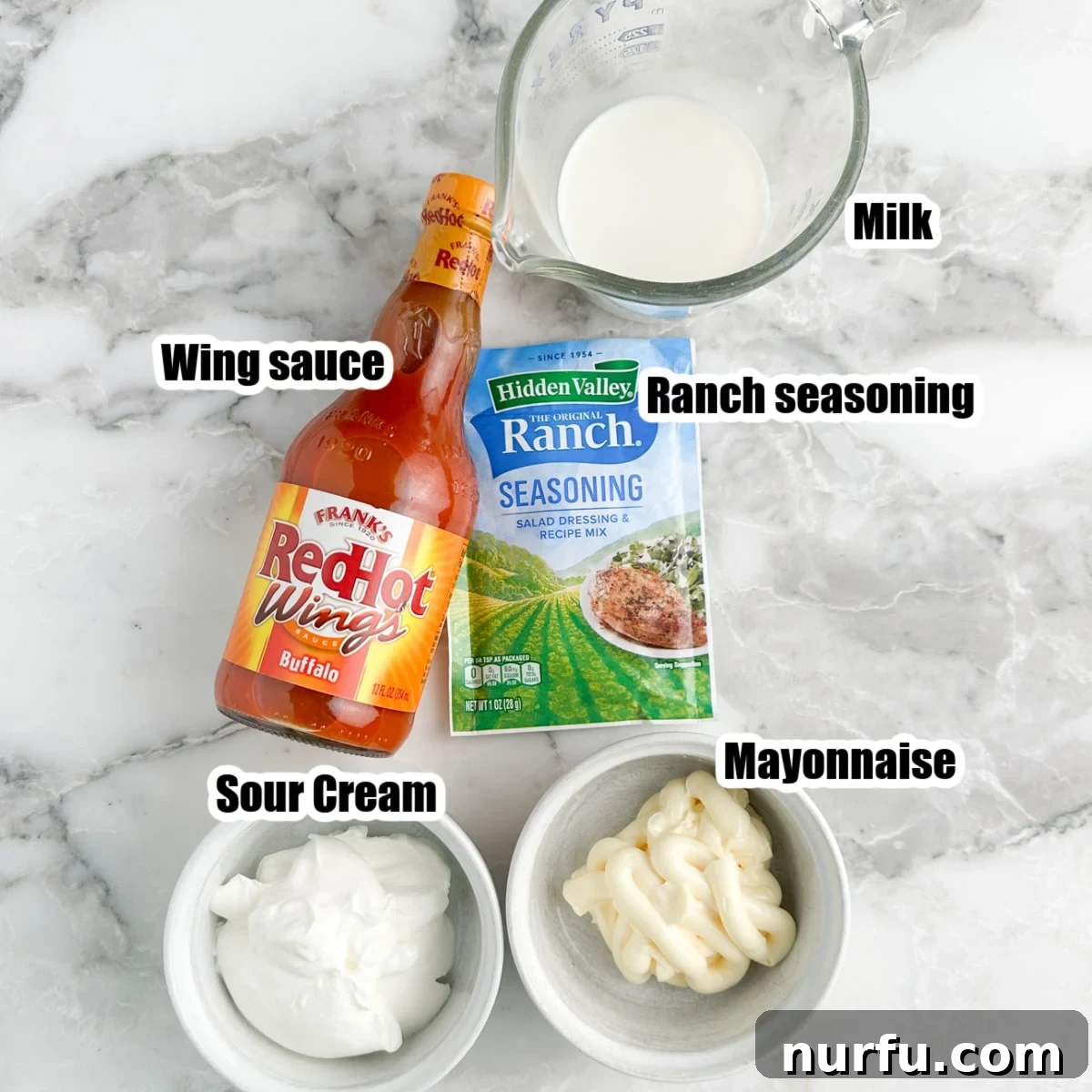 Individual bowls of sour cream, mayonnaise, milk, a bottle of buffalo wing sauce, and a packet of ranch seasoning on a rustic wooden surface, showcasing all the ingredients needed for buffalo ranch.