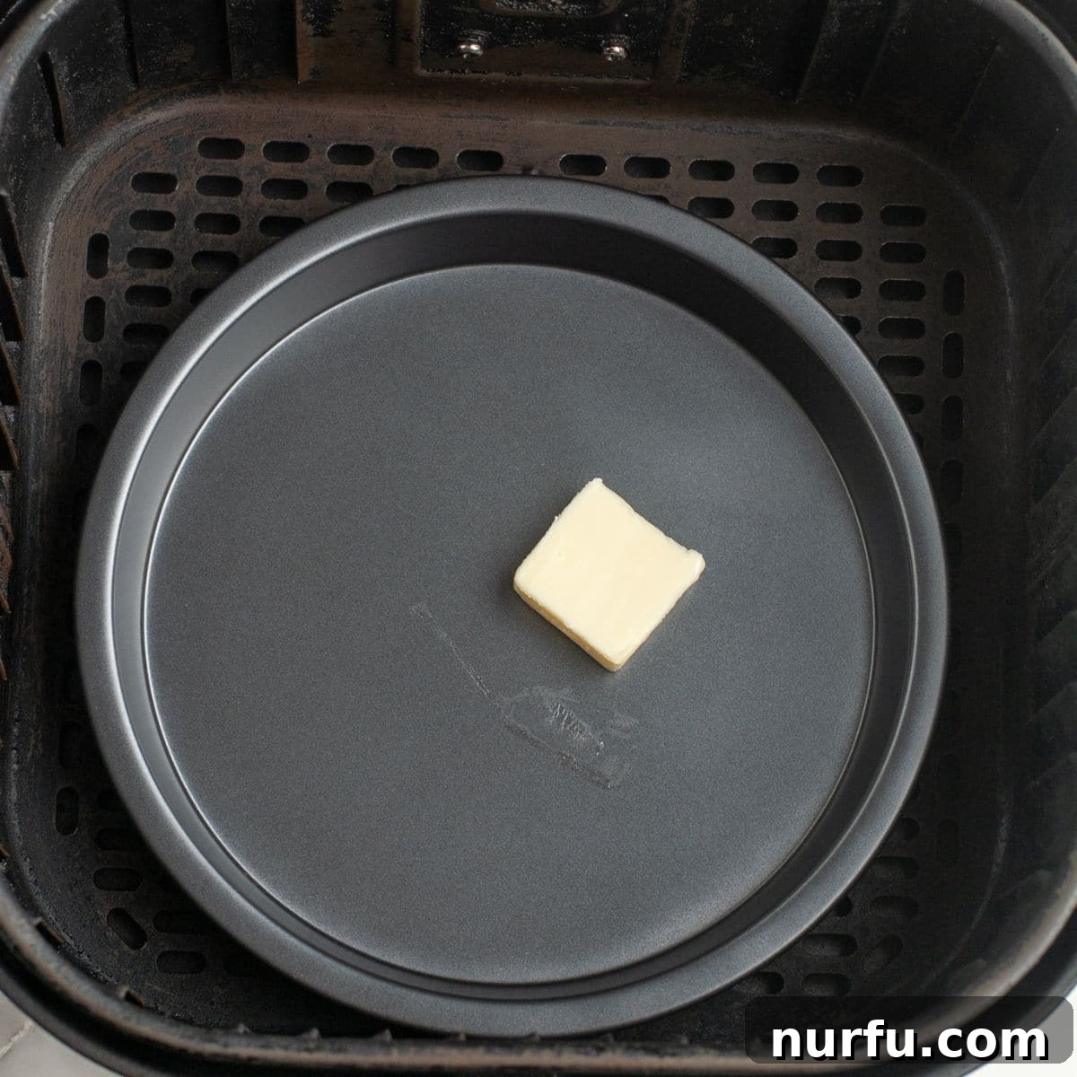 Golden & Crispy Air Fryer Fried Eggs 3 Small pan with melted butter sitting inside an air fryer basket, ready for eggs.