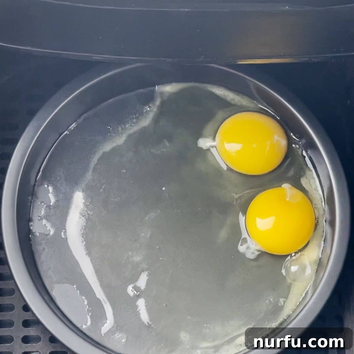 Golden & Crispy Air Fryer Fried Eggs 4 Two eggs cracked into a pan inside an air fryer basket, beginning to cook.