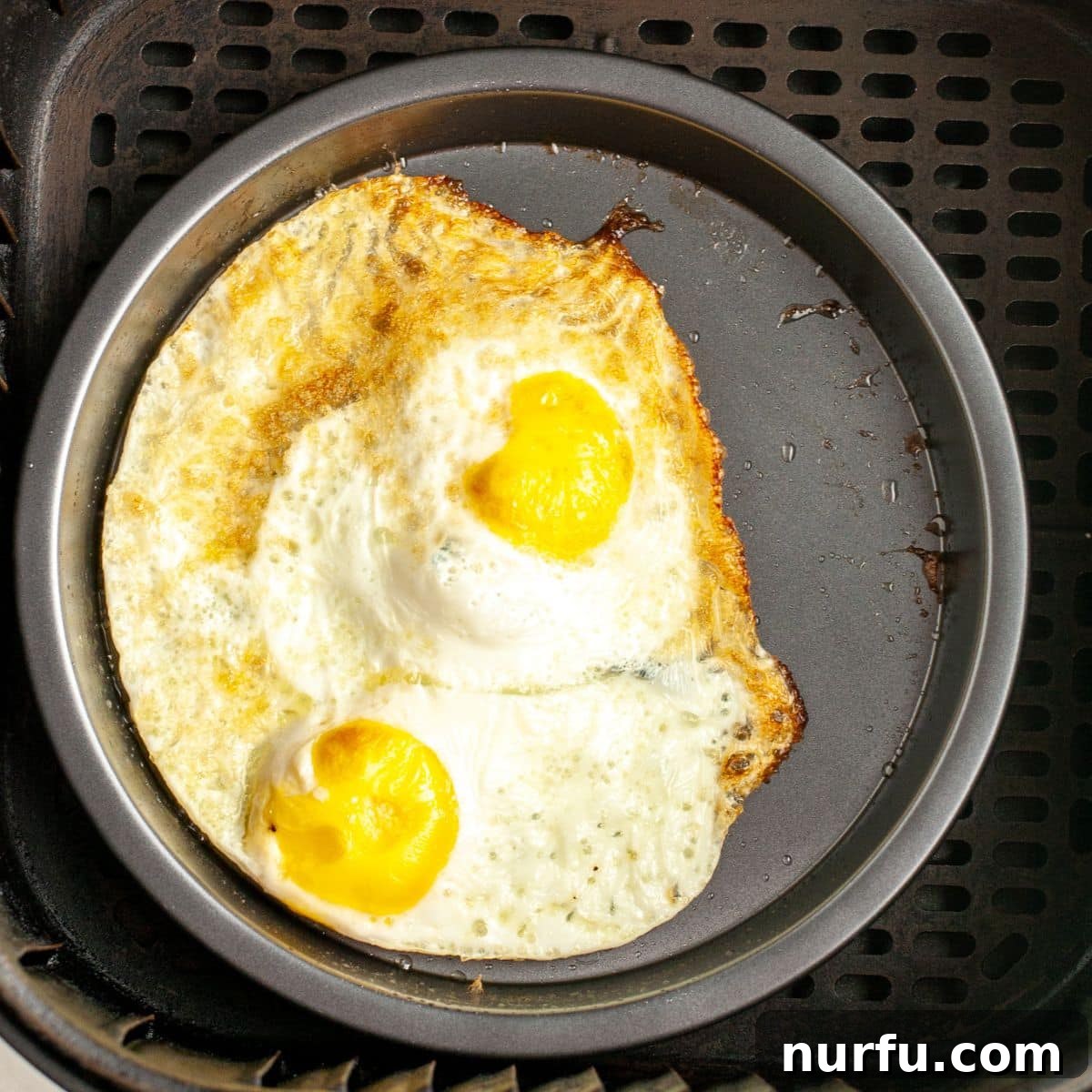 Golden & Crispy Air Fryer Fried Eggs 5 A pan with two perfectly fried eggs, freshly cooked and ready for seasoning.
