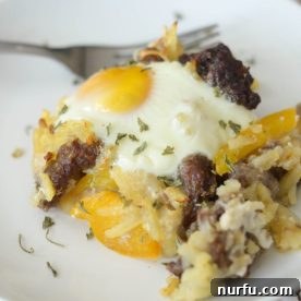A hearty breakfast casserole served on a plate, brimming with eggs, hash browns, sausage, and peppers.