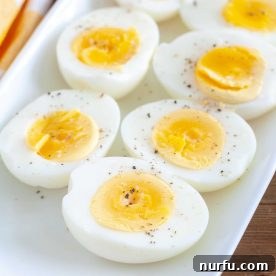 Perfectly hard-boiled eggs, cut in half and arranged on a white plate, showcasing their creamy yolks.