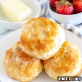 Three golden biscuits served on a plate, alongside a small bowl of butter and fresh strawberries.
