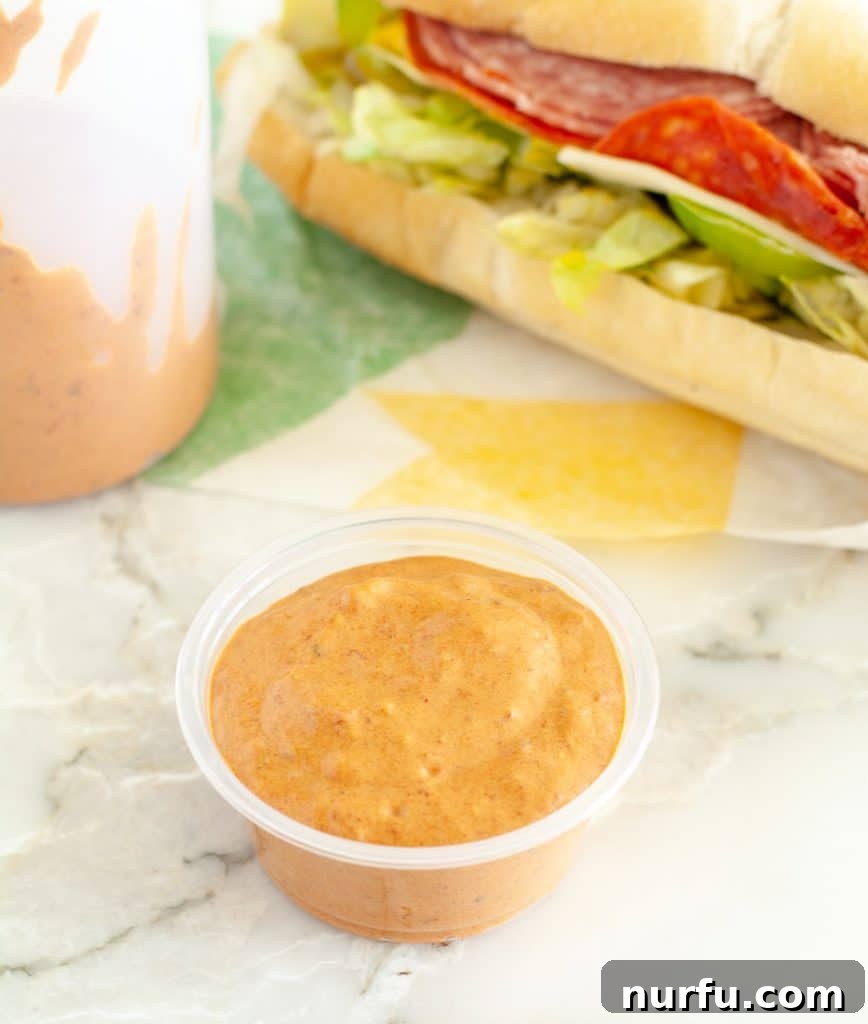 Crack the Code: Subway's Chipotle Sauce Recipe 2 A cup of creamy, zesty Subway Chipotle Southwest Sauce next to a freshly made sandwich, showcasing its vibrant flavor.
