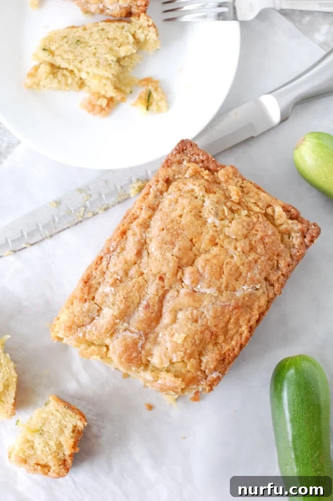 A slice of zucchini bread on a plate with a fork, next to a loaf of zucchini bread and a knife on a wooden table.