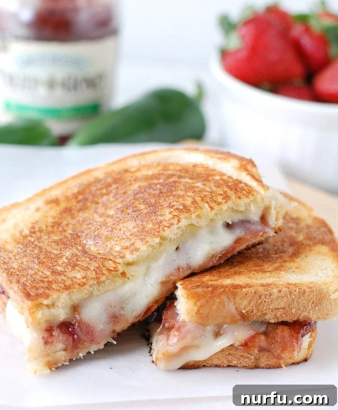 Strawberry Jalapeno Bacon Melt 2 Golden brown grilled cheese sandwich, cut in half, revealing melted cheese and strawberry jalapeno spread, served on a rustic plate.