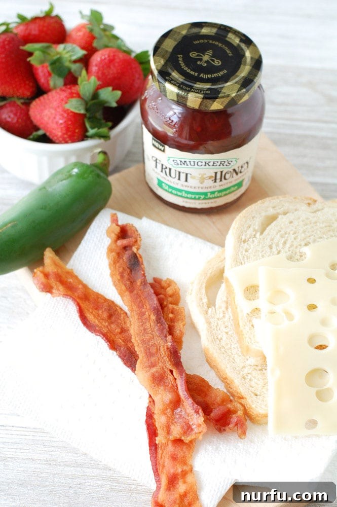 Strawberry Jalapeno Bacon Melt 3 Close-up of a Strawberry Jalapeno Bacon Grilled Cheese Sandwich, highlighting the gooey Swiss cheese and crispy bacon. The sandwich rests on a cutting board, ready to be enjoyed.