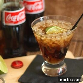 Several bottles of Coke with a glass containing a Rum and Coke cocktail, showcasing the drink and its key ingredient.