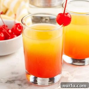 Shot glass filled with a layered drink and a bowl of cherries.