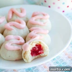 Cookies with pink frosting and a cherry in the middle, beautifully presented on a plate.