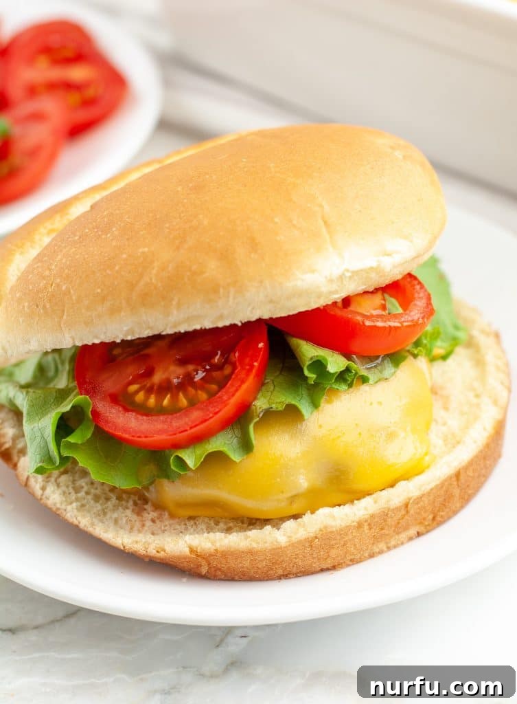 Perfect Oven Burgers 4 Cooked cheeseburger on a bun, garnished with fresh lettuce and tomato, ready to be served.