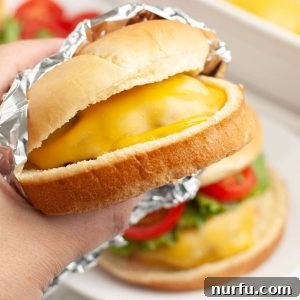 Hand holding a juicy cheeseburger, hot and ready to eat.