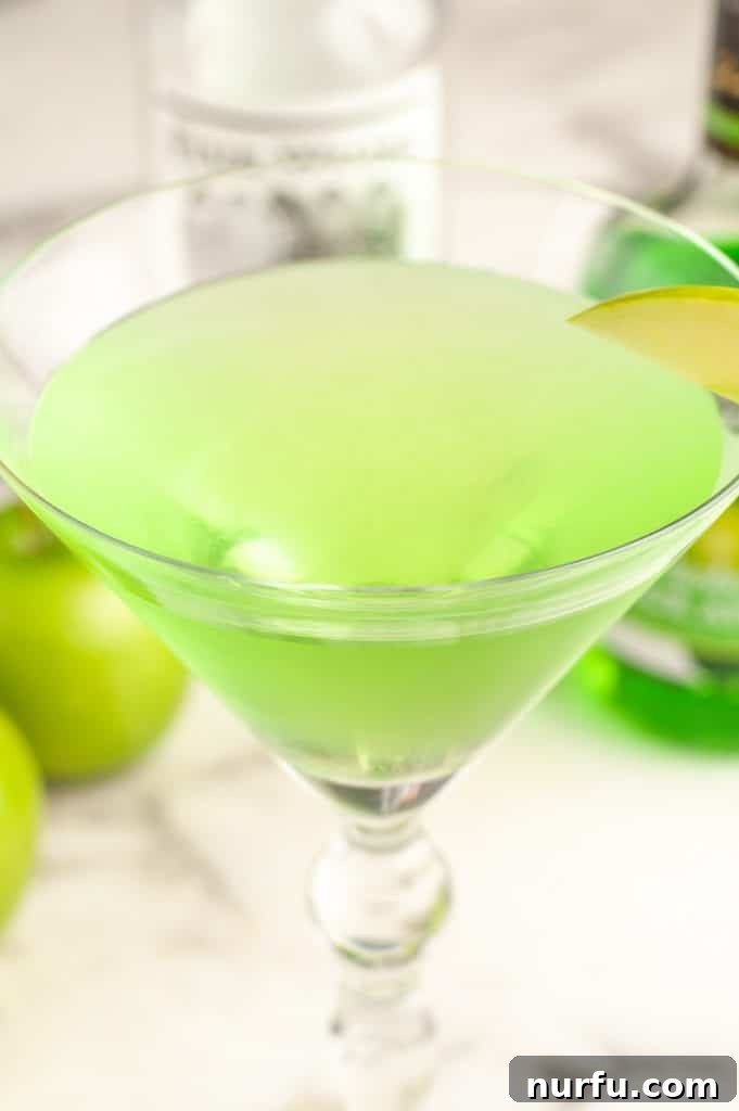 Master the Appletini: Simple Steps to a Tart Apple Martini 4 A freshly made green Appletini in a chilled martini glass, garnished with a green apple slice, against a soft-focus background.
