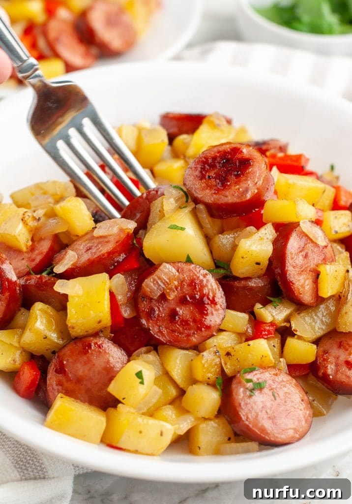 A fork picking up a piece of perfectly cooked Polish sausage and a tender potato cube from a cast iron skillet.