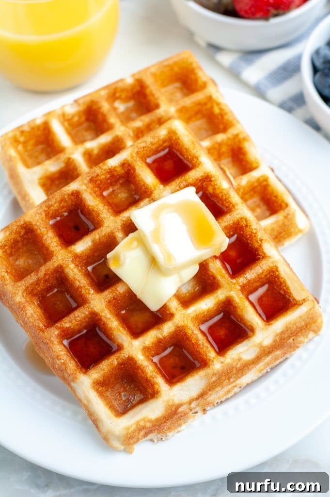 Fluffy Bisquick Waffles Made Easy 6 A plate of golden Bisquick waffles served with a glass of fresh orange juice and a bowl of mixed berries, creating a wholesome breakfast spread.
