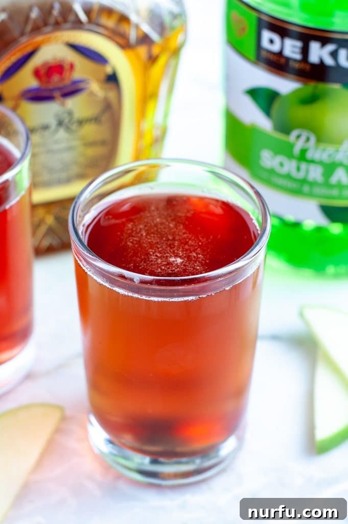 Signature Washington Apple Shot 2 Glass filled with a vibrant red Washington Apple Shot, garnished with an apple slice.