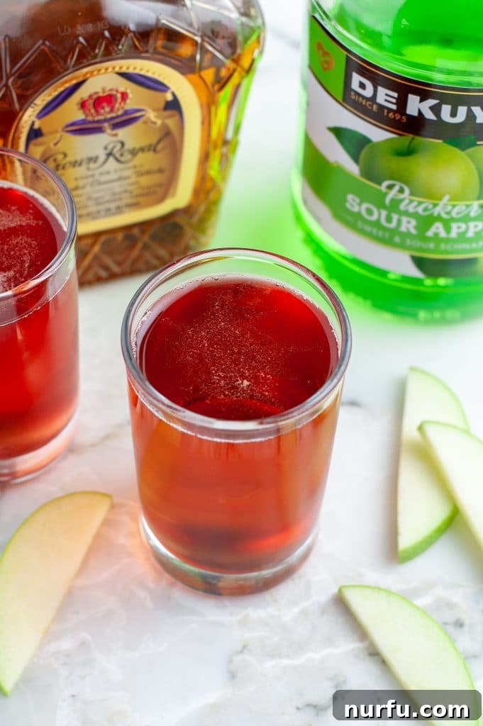 Signature Washington Apple Shot 5 Bottles of liquor (whisky, schnapps) next to a shot glass filled with the mixed Washington Apple Shot.