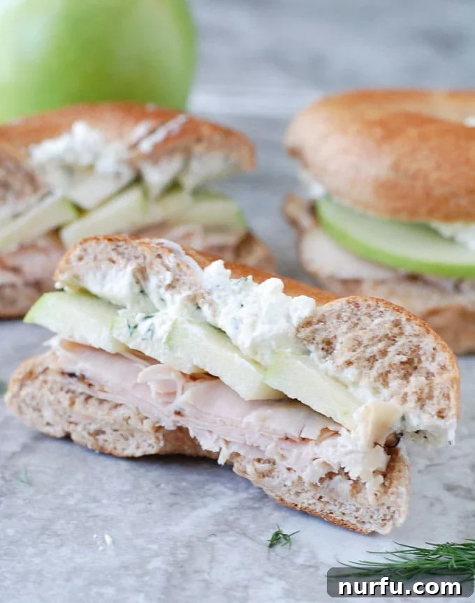 Sandwich Ready to Eat A perfectly assembled turkey apple bagel sandwich, neatly sliced in half to reveal its appealing layers and ready to be enjoyed.