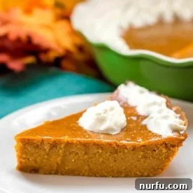Crustless pumpkin pie with a small dollop of whipped cream on top on a white plate. A Green Pie Dish can be seen in the left back corner