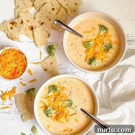 2 white bowls of Broccoli Cheddar Soup garnished with cheese and broccoli.