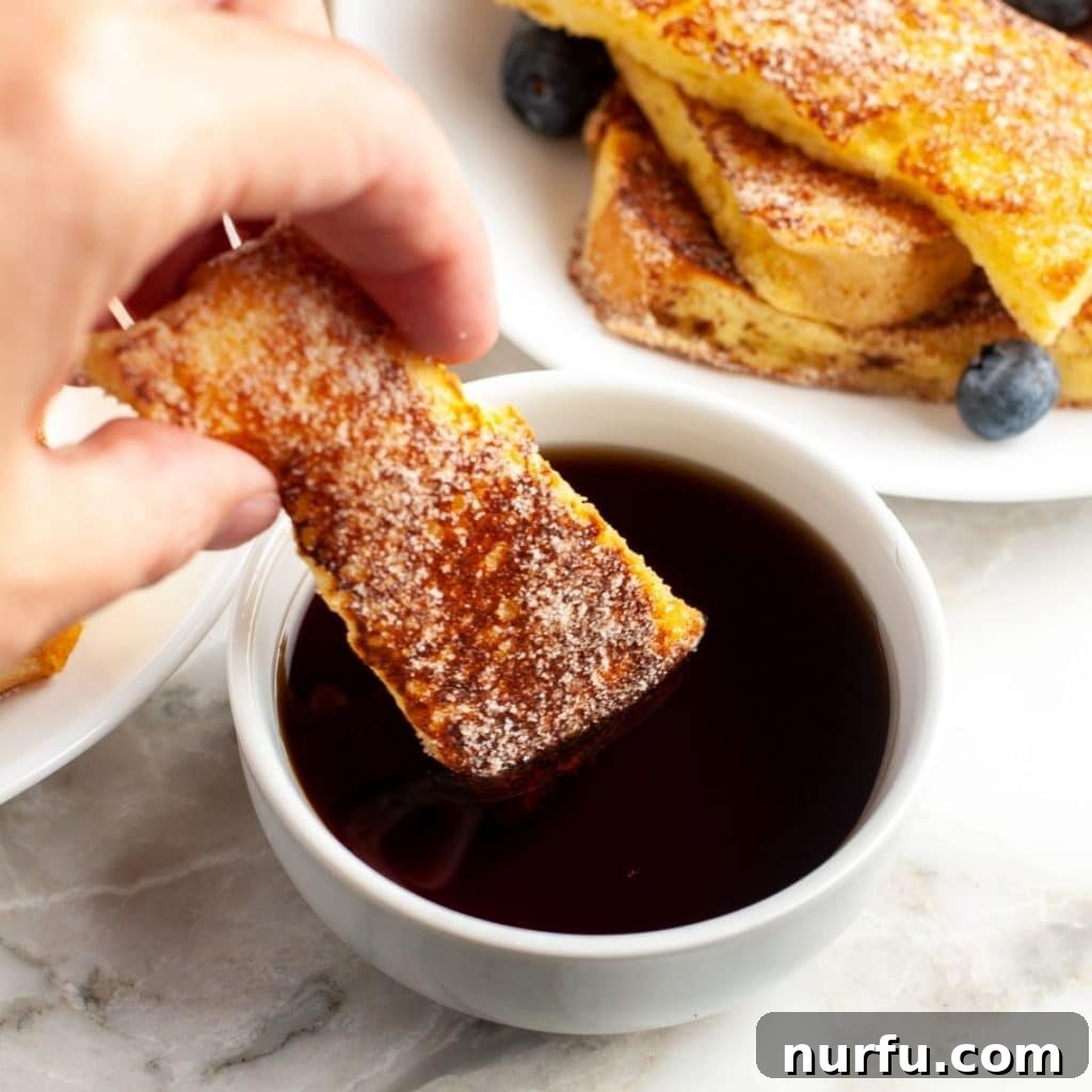 Golden French Toast Dippers 5 Close-up of a hand holding a single homemade french toast stick, perfectly coated and ready to dip.