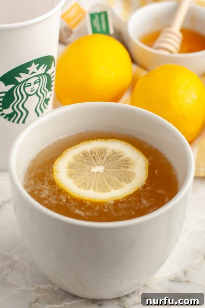 Starbucks Soothing Elixir 2 A steaming mug of homemade Starbucks Medicine Ball Tea, garnished with a lemon slice, sits on a rustic wooden surface.