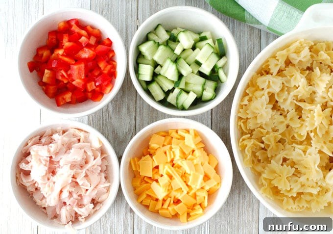 Fresh ingredients laid out for making pasta salad, including pasta, vegetables, and deli meats.