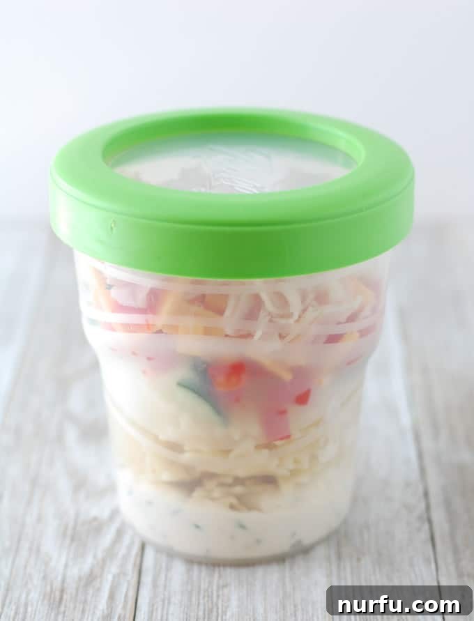 A mason jar pasta salad, with all ingredients mixed, ready to be eaten from the jar.