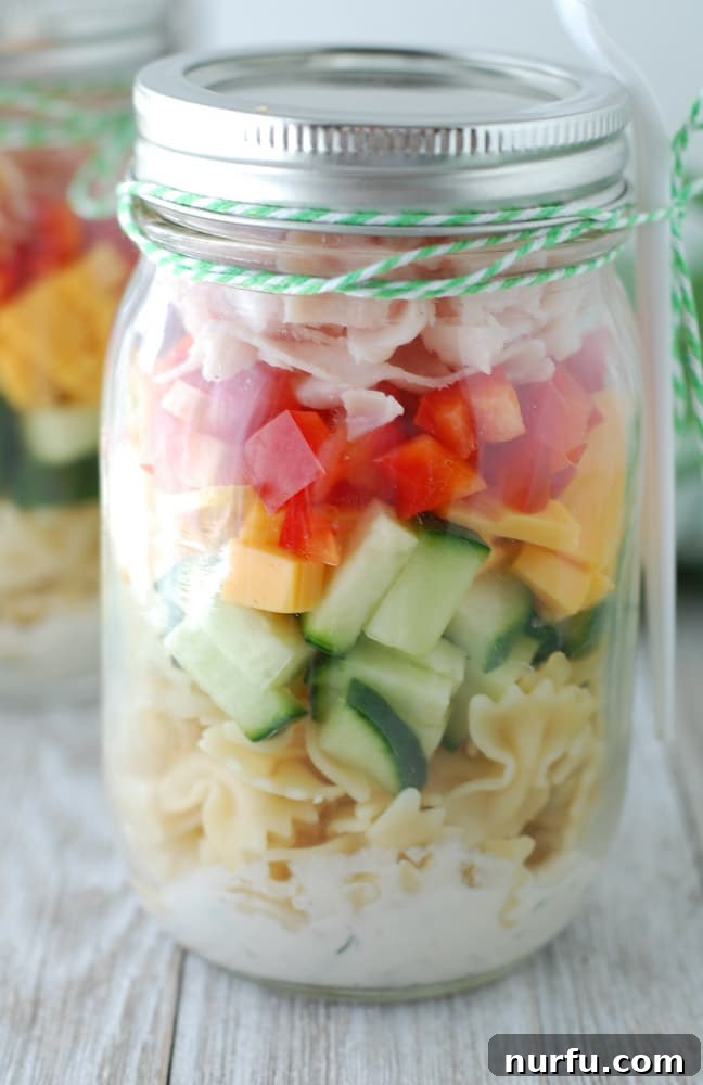 Seven mason jars lined up, each filled with a different, vibrant pasta salad combination, showcasing meal prep variety.