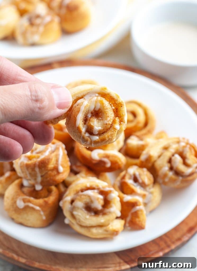 King's Cinnamon Crunch 5 A hand holding a mini cinnamon roll, showing its small size and icing.