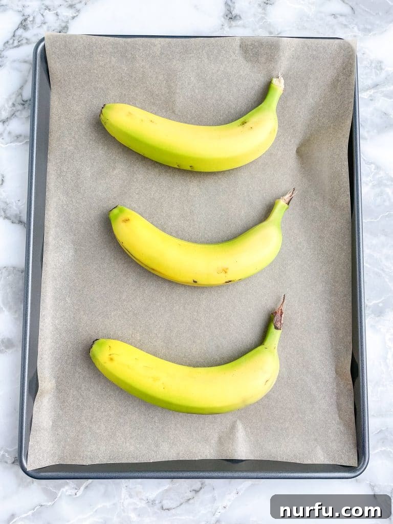 Four Simple Methods to Ripen Bananas Fast 3 Three unpeeled bananas laying on a lined baking sheet before baking.