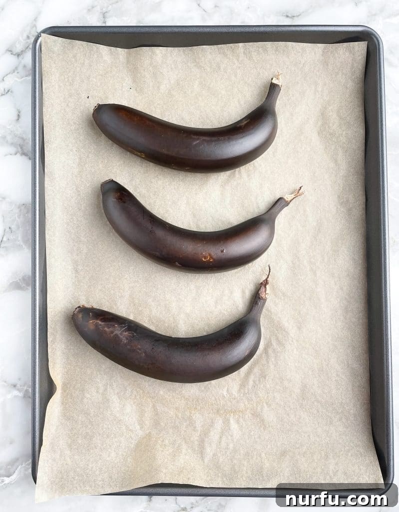 Four Simple Methods to Ripen Bananas Fast 4 Black, oven-ripened bananas laying on a lined baking sheet.
